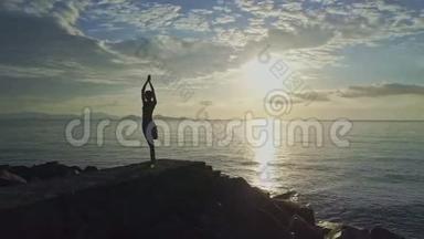 女孩<strong>剪影瑜伽</strong>在岩石上对抗海洋上空升起的太阳